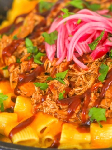 BBQ Smoked Chicken over mac and cheese topped with pickled red onions and garnished with sliced scallions in cast iron skillet.