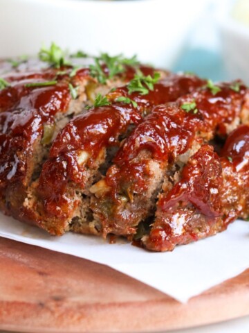 Final image of meatloaf sliced and served on top of parchment paper underneath a wooden cutting board.