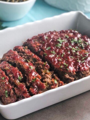 Herb meatloaf with sweet heat chili sauce in a ceramic loaf pan.