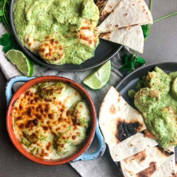 Flatlay with blue round bowl with shrimp in roasted poblano cream sauce. two gray plates with scooped out shrimp in sauce with warm tortillas.