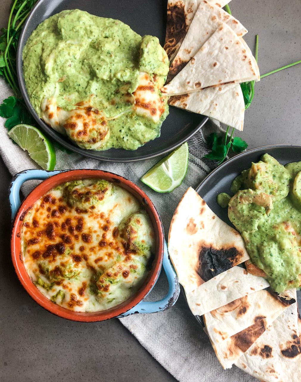 Flatlay with blue round bowl with shrimp in roasted poblano cream sauce. two gray plates with scooped out shrimp in sauce with warm tortillas.