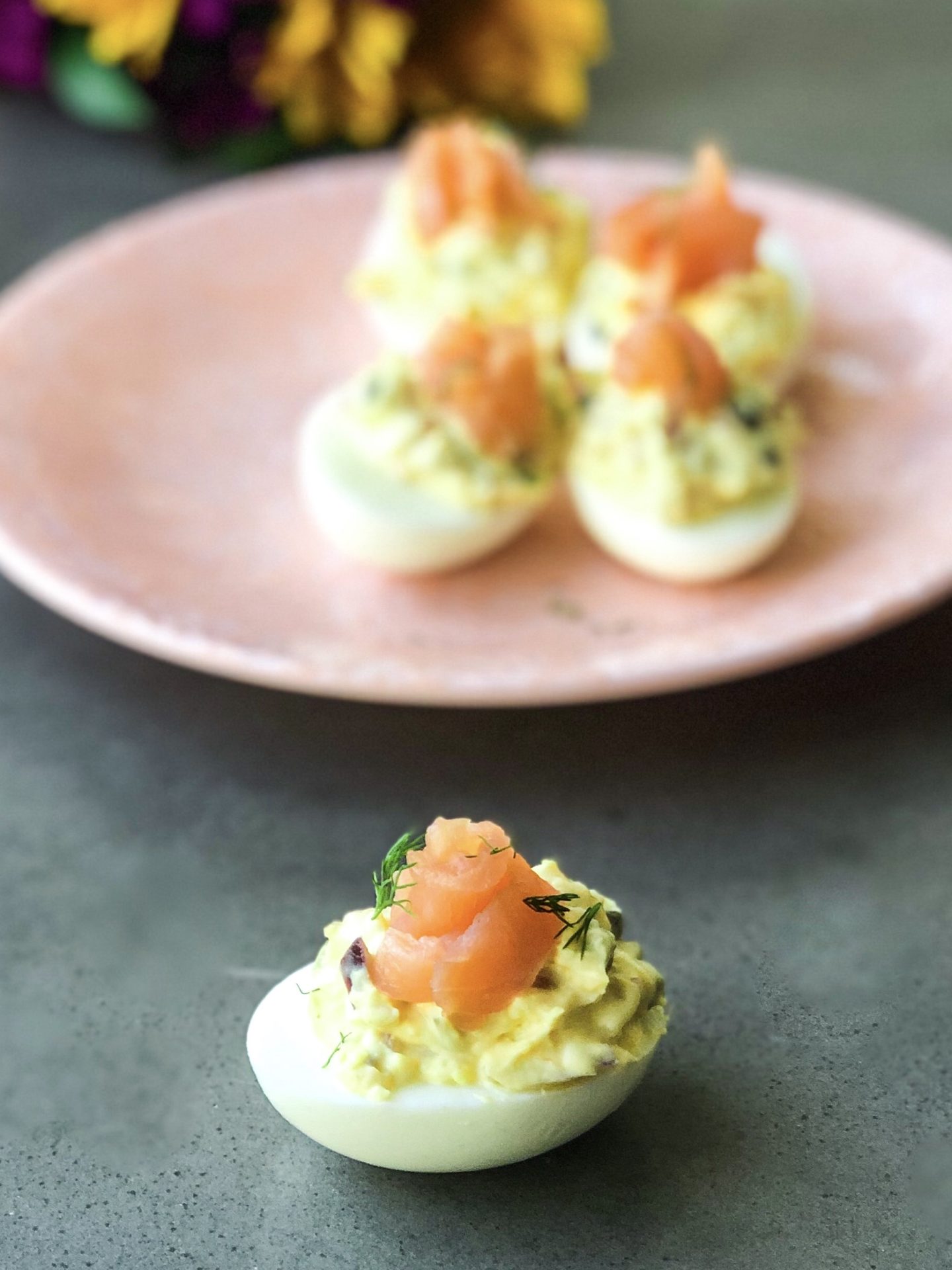 a smoked salmon deviled egg on a surface with a plate of more in the background