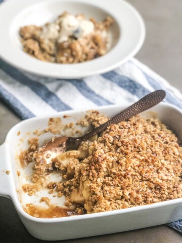 Apple Crumble in baked dish, scooped out and plated on a bowl behind the baked dish that's out of focus. Blue and white striped towel underneath the dishes to add style.