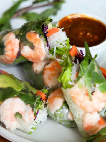 Featured image of shrimp spring rolls plated on a gray matte plate with one spring roll sliced in half, showing contents of the inside ingredients.