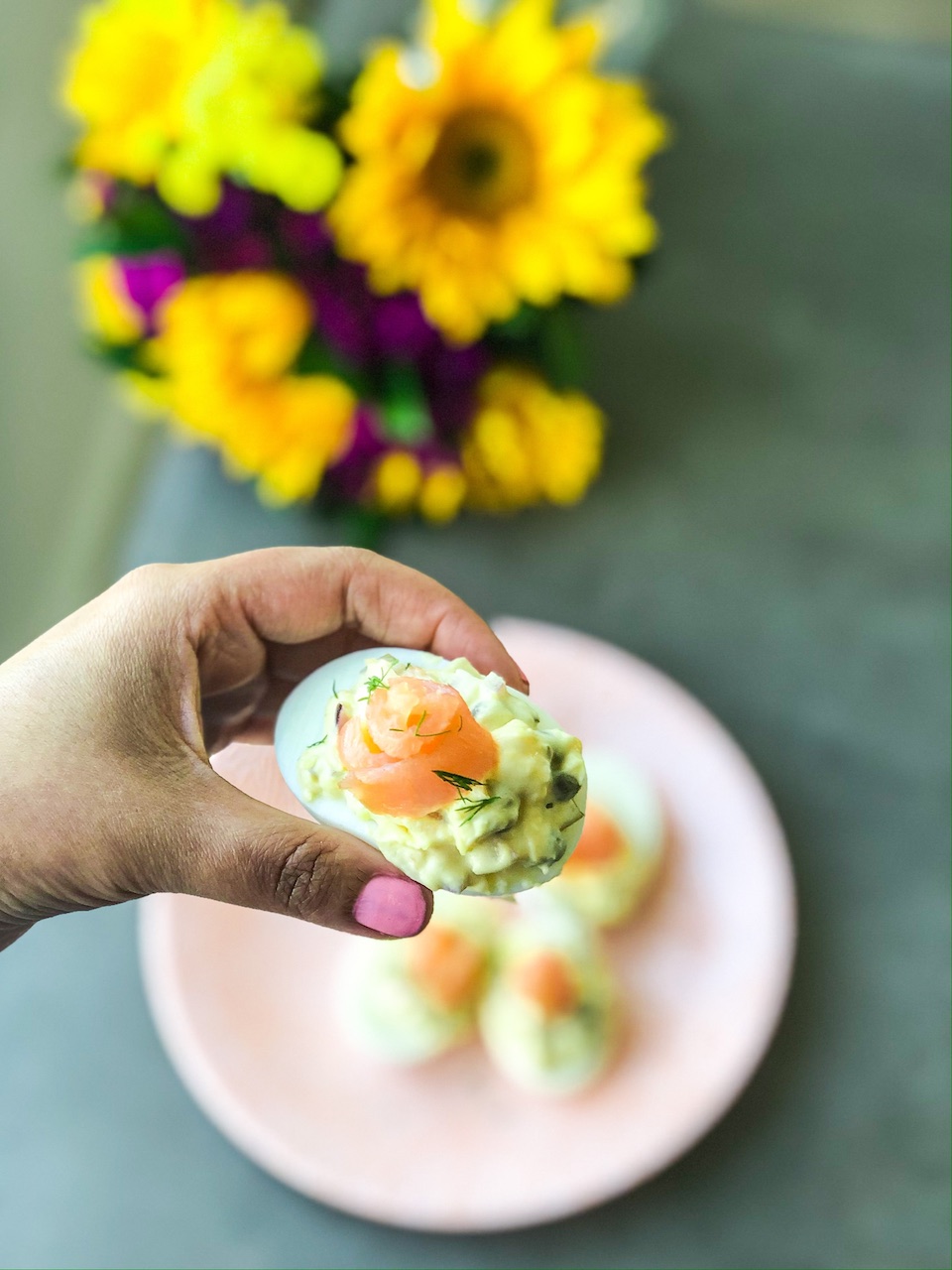 a hand holding one smoked salmon deviled egg over a plate of even more