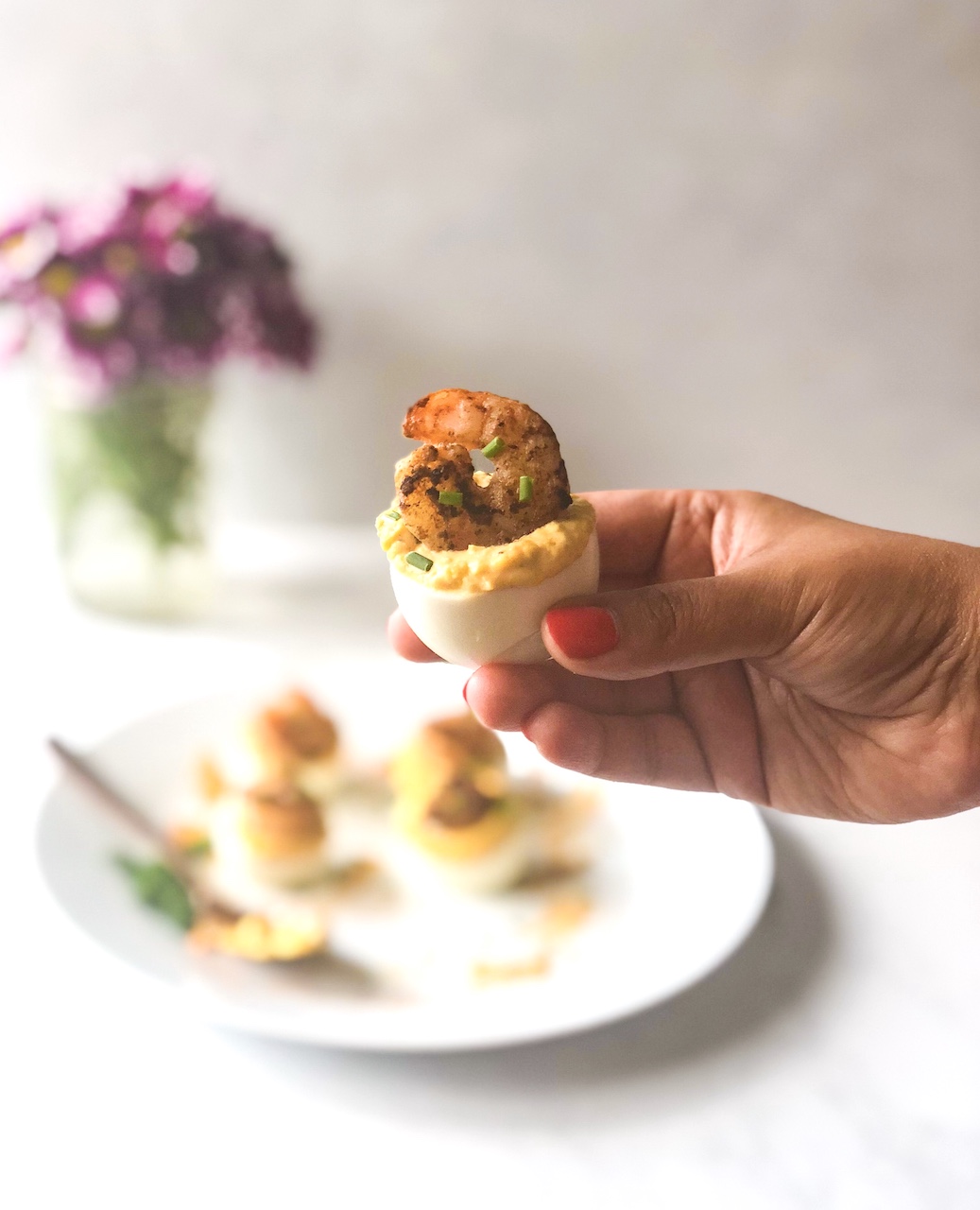 cajun deviled eggs a hand holding a cajun shrimp deviled egg with more plated in the background