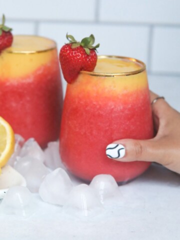 Hand with designer nail holding wine slushy with ice and sliced lemons used for styling purposes.