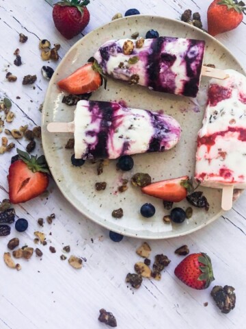 Three frozen berries parfait pops platted with strawberries and blueberries.