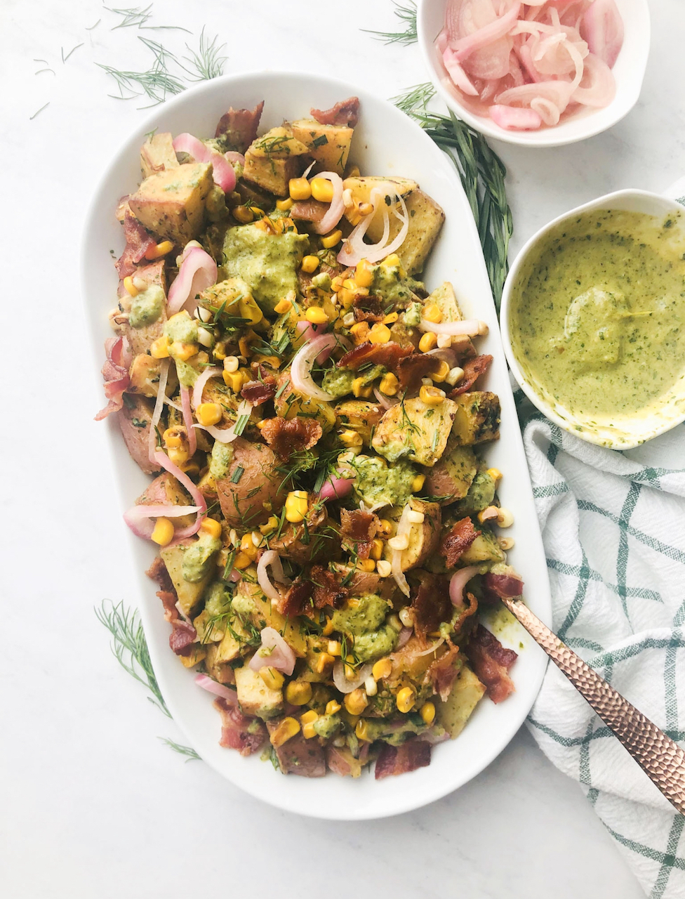 a platter of warm potato salad with a side of pickled shallots and creamy poblano sauce