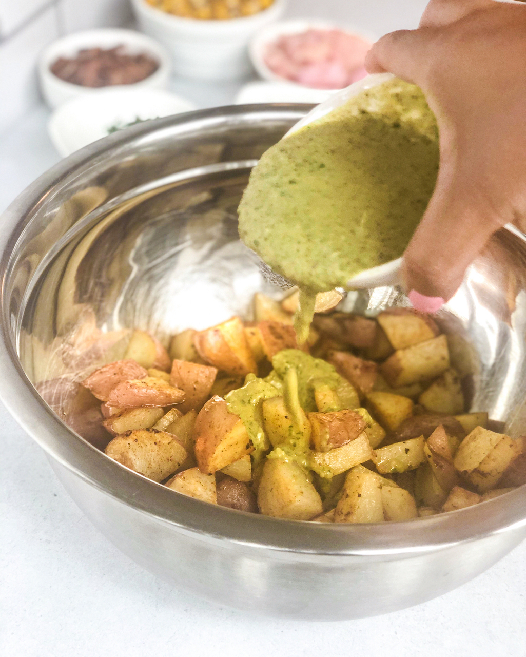 pouring poblano sauce over diced roasted potatoes