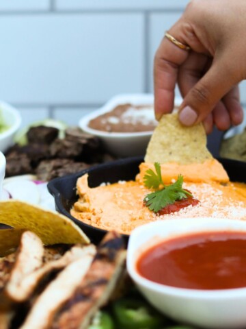 Featured image for nacho board with image of final recipe with hand dipping cheese sauce.