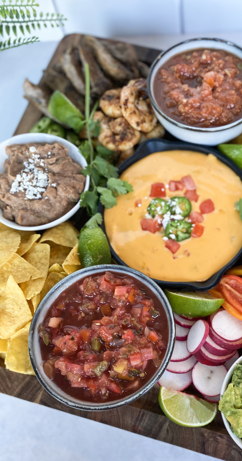 close up view of a Mexican charcuterie board that contains tortilla chips, refried beans, queso dip, salsa, carne asada, and grilled shrimp