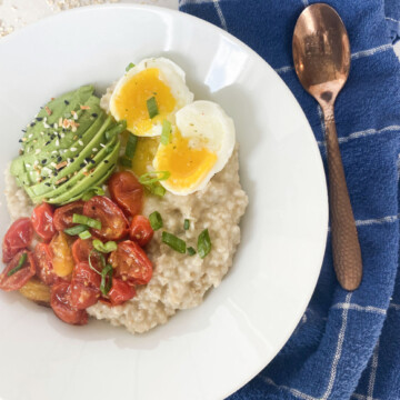 White bowl with oatmeal topped with avocado, tomato, soft boiled eggs decorated with a blue decorative towel.