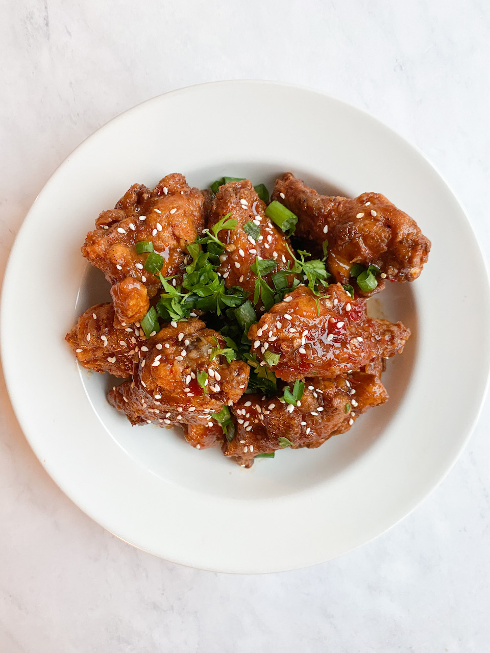 White bowl with fried sweet chili orange chicken wings topped with fresh cilantro and green onion.
