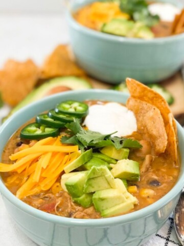 Creamy Chicken Tortilla Soup topped with avocado slices, shredded cheddar cheese, jalapeno peppers, sour cream and tortilla chips.