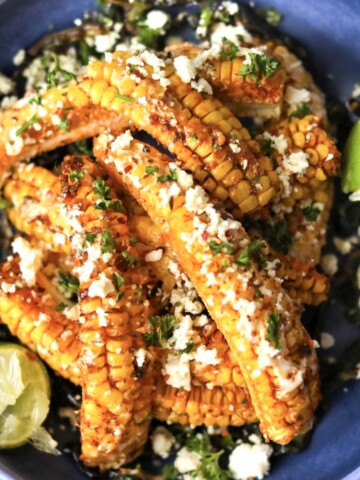 Elotes corn ribs in a blue plate topped with cotija cheese and cilantro.