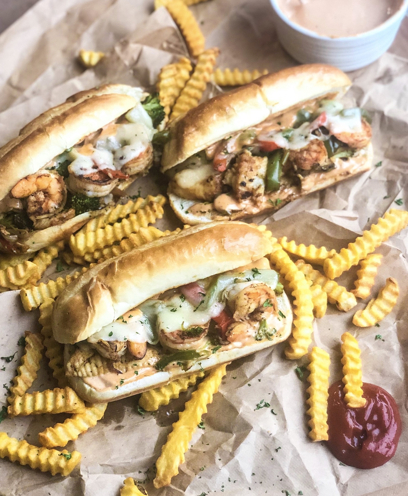 Three Seafood Cheesesteaks with Remoulade Sauce and sauteed veggies. Styled with crinkle cut fries, ketchup and remoulade sauce in a sauce cup.
