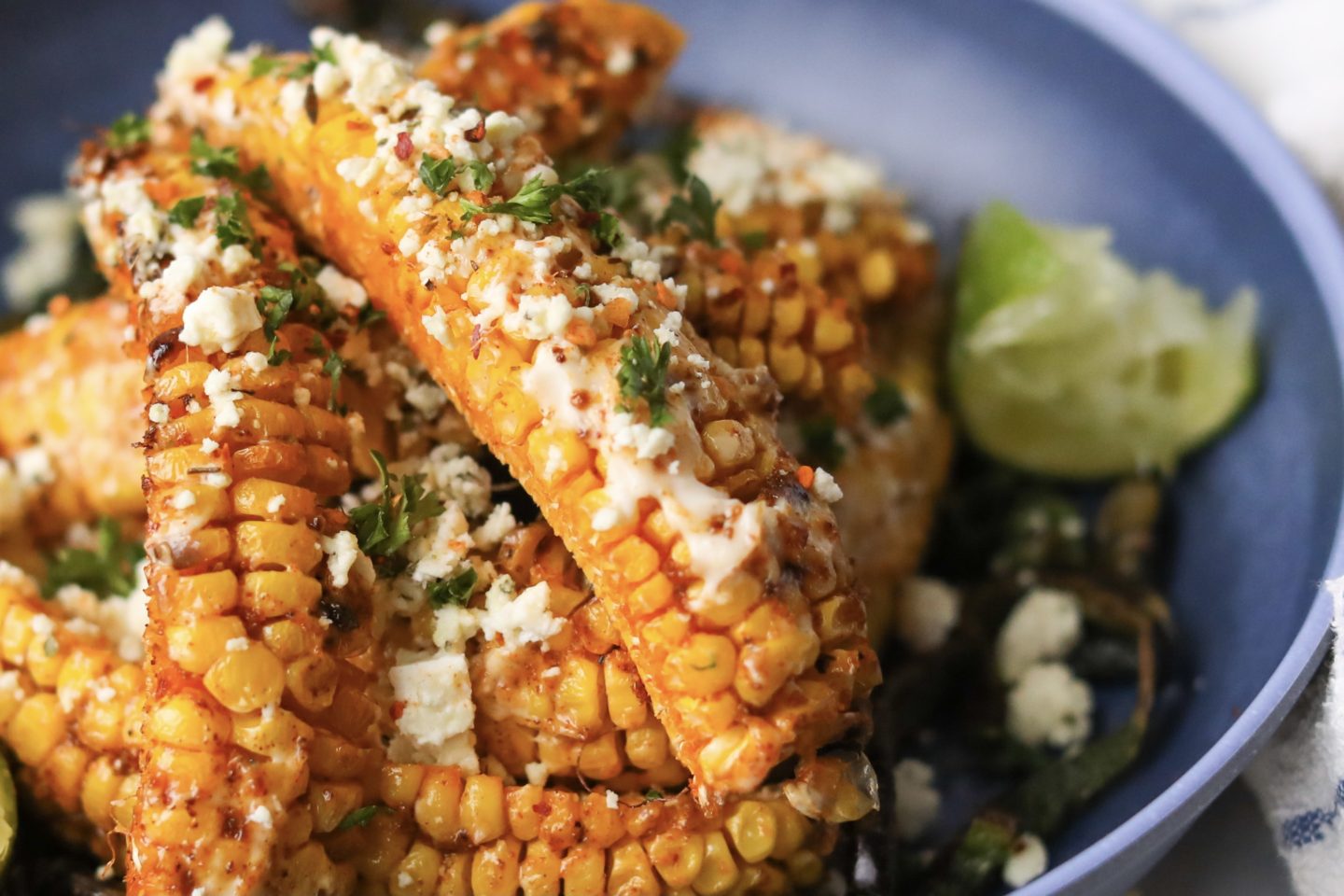 Tik Tok Trend Corn Ribs piled onto a blue bowl with one corn "rib" in focus. Styled with sliced poblano peppers on the bottom and a squeezed wedge of lime.