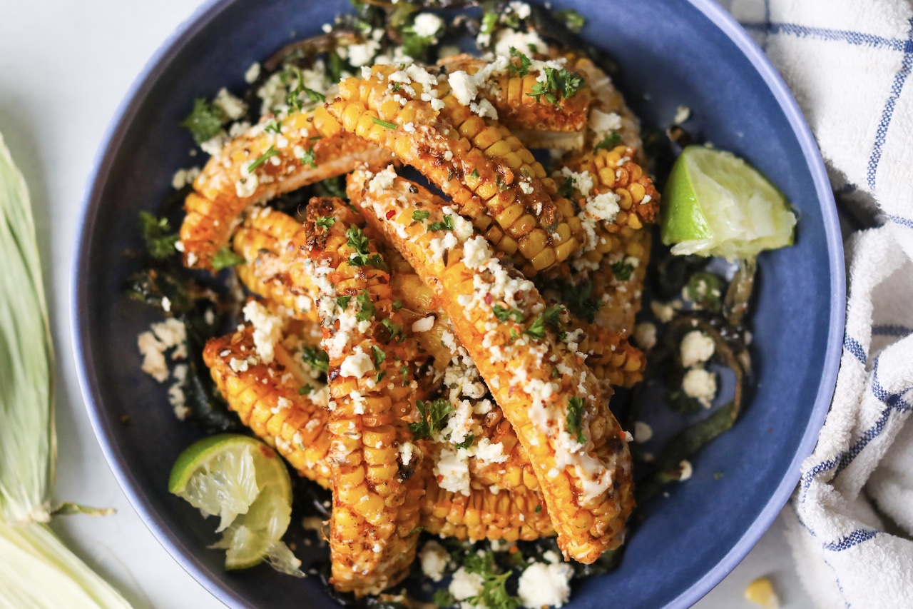 Tik Tok Trend Corn Ribs piled onto a blue bowl with with top down focus. Styled with sliced poblano peppers on the bottom and two wedges of lime.