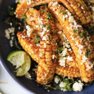 Tik Tok Trend Corn Ribs piled onto a blue bowl with multiple corn "ribs" in focus. Styled with sliced poblano peppers on the bottom and two wedges of lime.