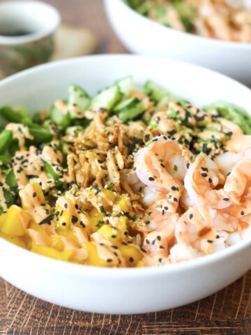 Dragon roll sushi bowl in a white bowl topped with shrimp, mango, jalapeno, avocado.