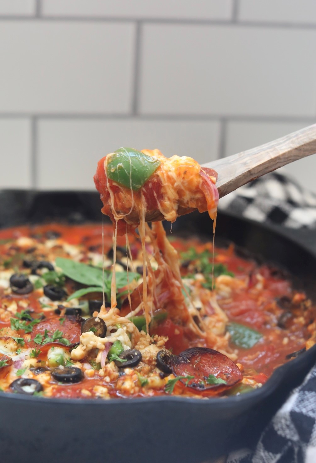close up view of a wooden spoon hovering a skillet full of pizza casserole