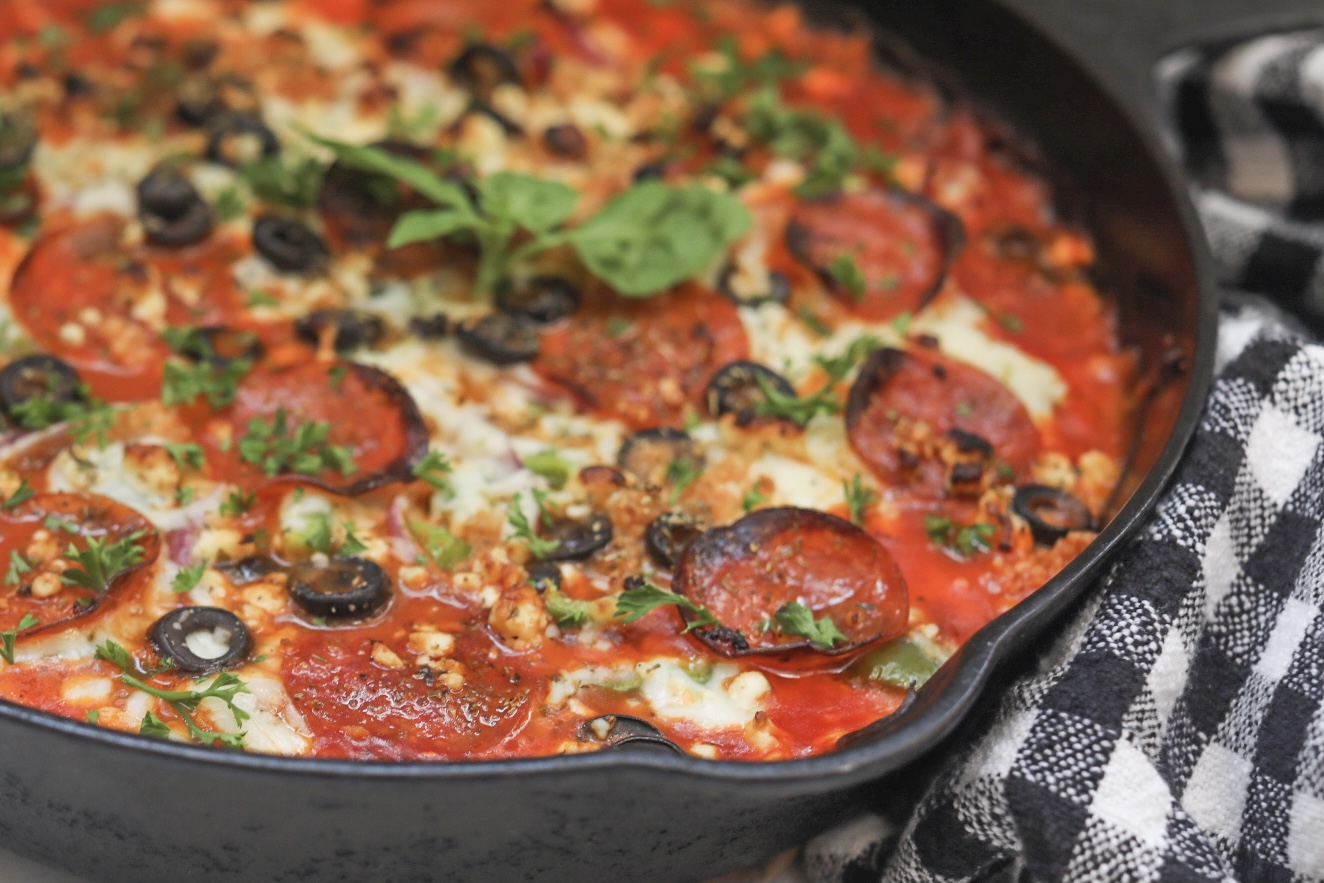 Black Cast Iron Skillet with Baked Crustless Pizza with pepperoni, cheese and olive toppings.