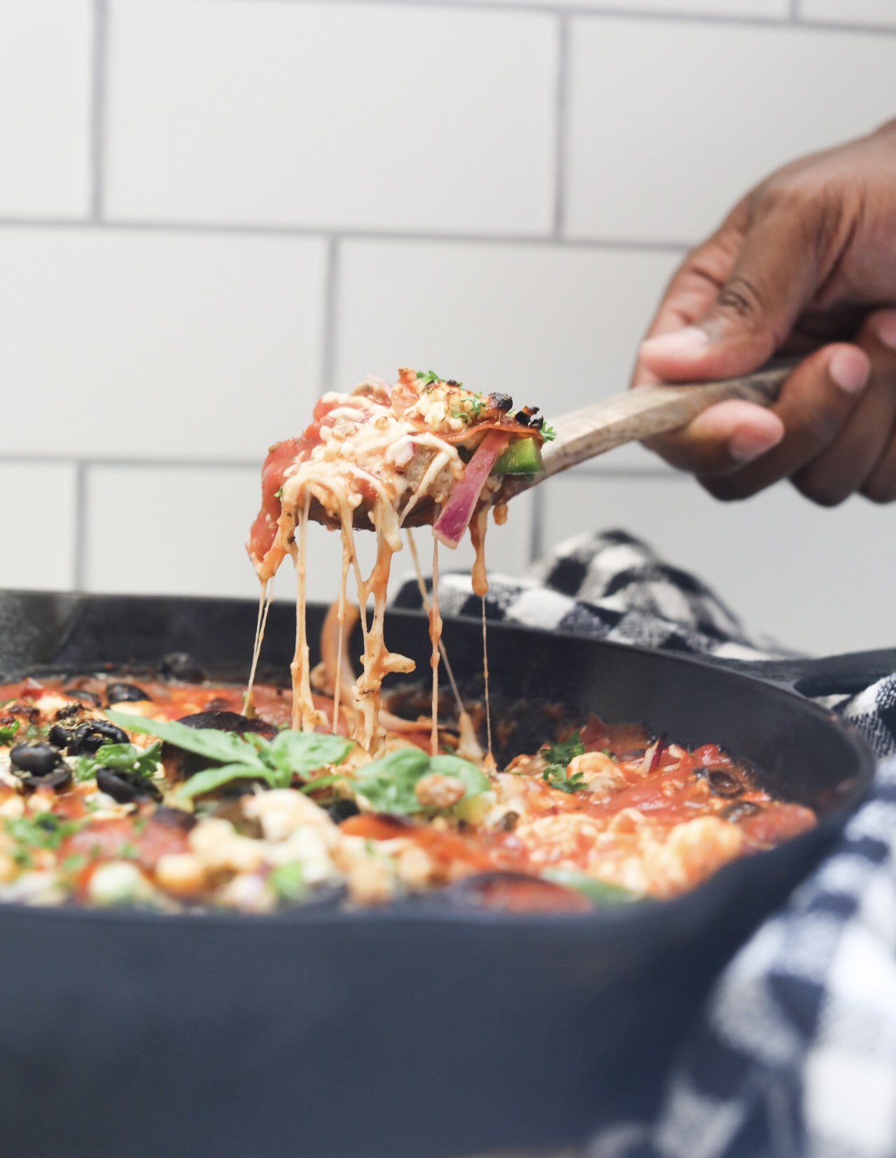 pizza casserole keto a hand holding a spoon over skillet with an excellent cheese pull