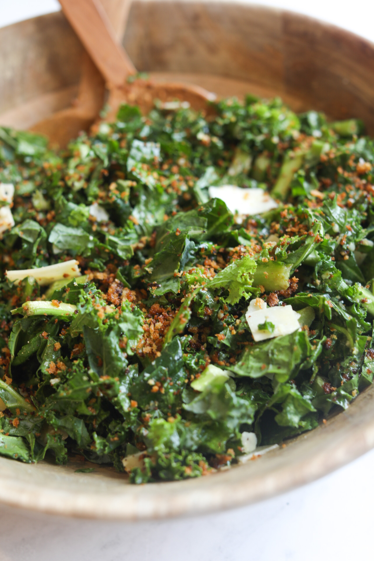 Savory Kale Salad with fresh parmesan cheese in a wooden salad bowl with wooden salad cutlery for styling purposes.