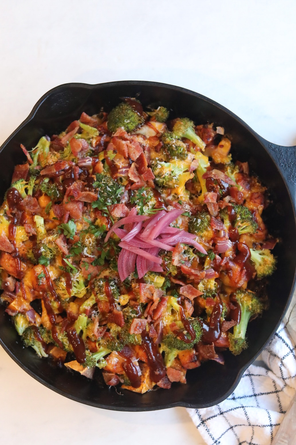BBQ Chicken Sweet Potato Skillet in a black iron cast skillet. Skillet dish includes sweet potatoes, chicken, broccoli, red onion, cilantro and topped with pickled red onions.