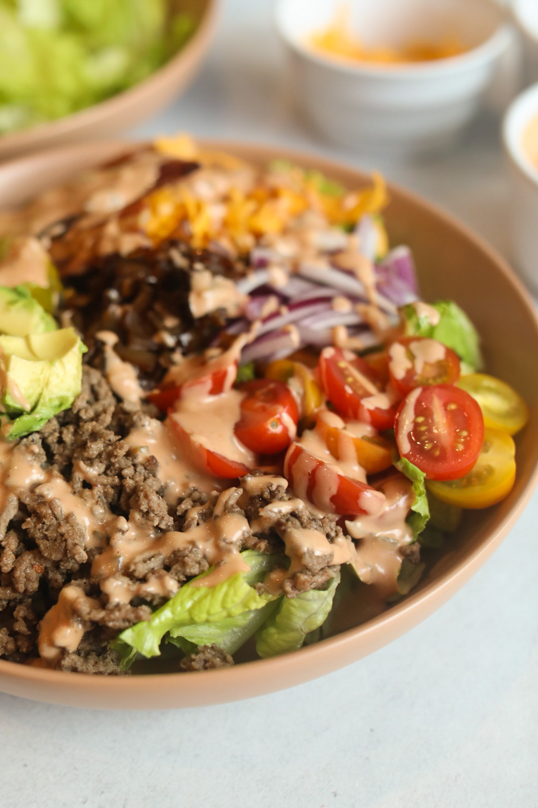 Bacon cheeseburger salad with vegetable toppings such as cherry tomatoes, red onion, cheddar cheese, bacon and avocado. Drizzled with burger sauce. 