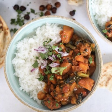 Chicken and Sweet Potato Curry with Coconut Milk in a small bowl with a light blue hue inside filled with jasmine rice and prepared curry mixture. Naan bread is added for styling purposes as well as a small wooden bowl with fresh herbs added.