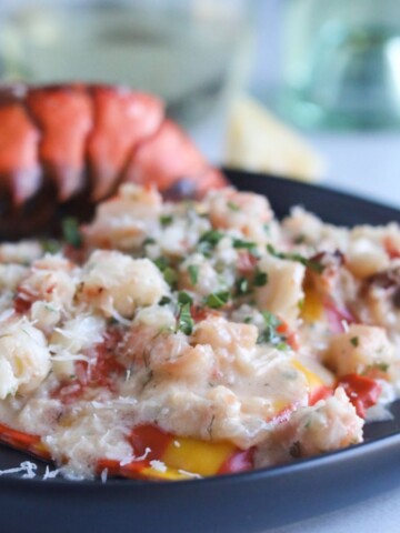 Lobster ravioli in a shrimp cream sauce on a black plate.