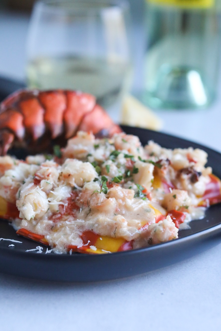 Lobster and shrimp ravioli completed dish on a black plate with Trader Joe's lobster ravioli that's striped in color with bright orange and yellow colors. Out of focus is a bright red lobster shell and a glass of white wine and the wine bottle for styling purposes.