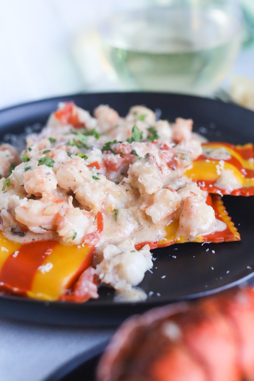 Lobster and shrimp ravioli completed dish on a black plate with Trader Joe's lobster ravioli that's striped in color with bright orange and yellow colors.