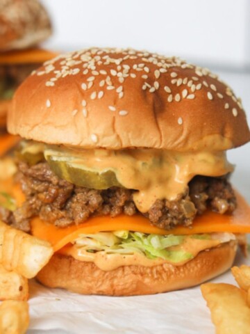 Big Mac Sloppy Joe finished recipe stacked with bun, lettuce, cheddar cheese, beef mixture, pickles, sauce and bun. Fries added for styling purposes.