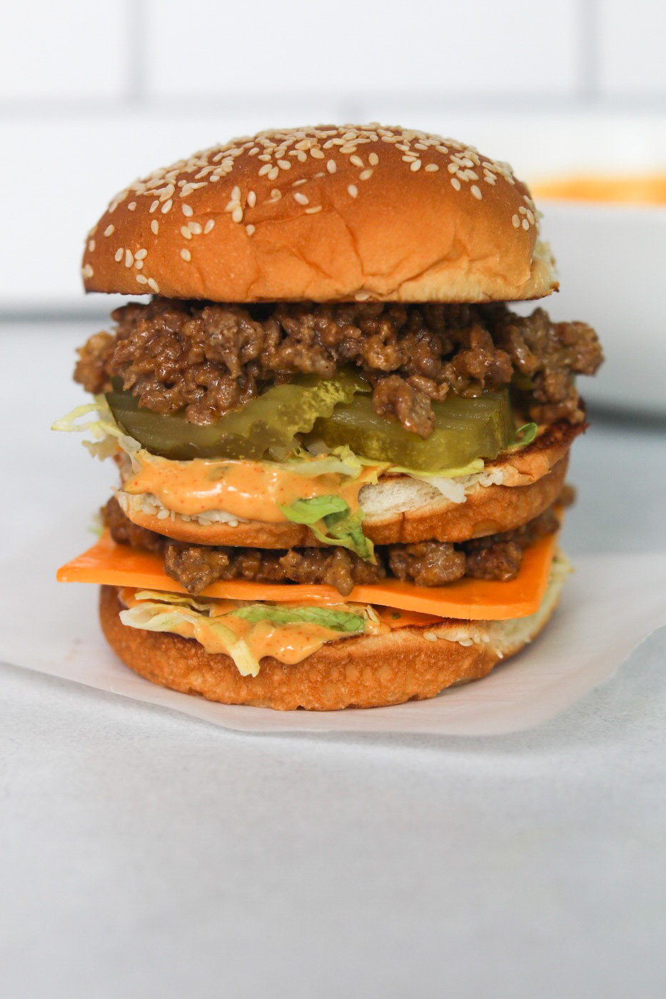 Burger in the center of the image with white background. Big Mac Sloppy Joe image with stacked burger that looks similar to a traditional Big Mac but with ground beef "sloppy joe" texture. Fries are added for styling purposes.