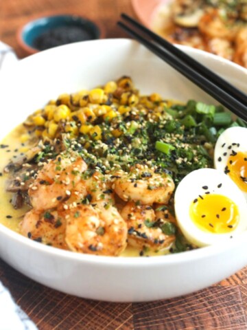 Cajun shrimp ramen served in a white bowl topped with shrimp, roasted corn, green onion and soft boiled eggs.