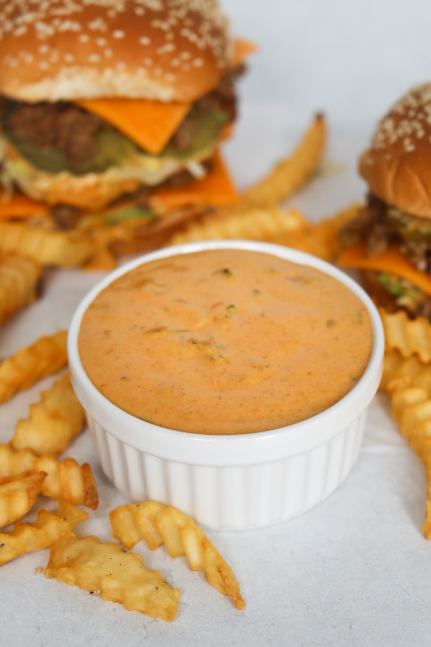 Homemade Big Mac Sauce in a white ramekin cup with two Big Mac Sloppy Joes and fries added for styling purposes.