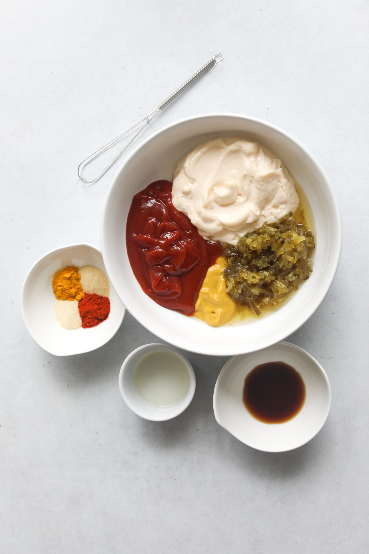 Homemade Big Mac Sauce ingredients shot. Ketchup, mayo, sweet relish and yellow mustard added in a white bowl with smaller white bowls added around the bowl.