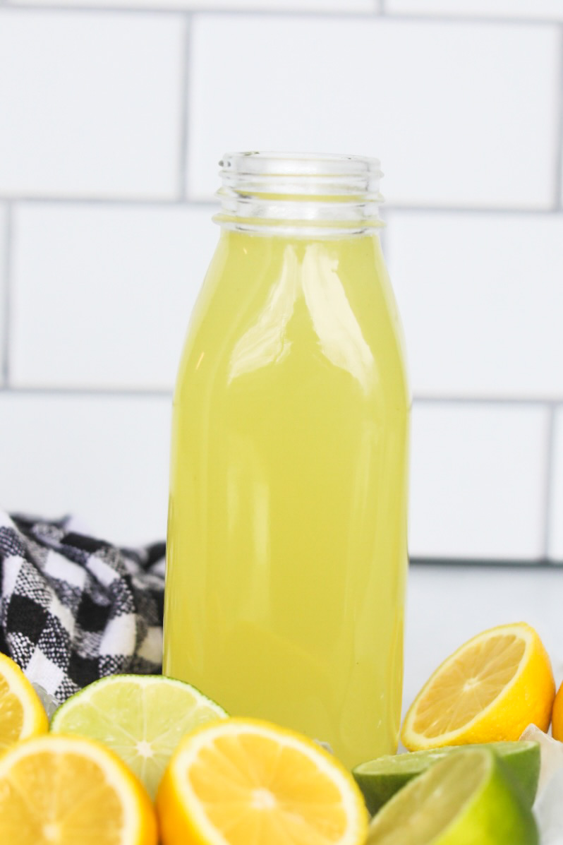 Homemade sour mix filled in a glass pint jar with sliced lemons and limes added for styling purposes. Black and white towel added for styling purposes.