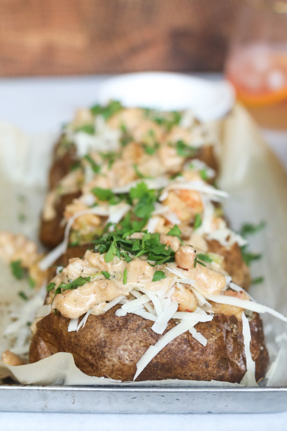 Four baked potatoes baked and topped with Cajun shrimp cream sauce. Baked potatoes are topped with additional shredded cheese and fresh parsley.