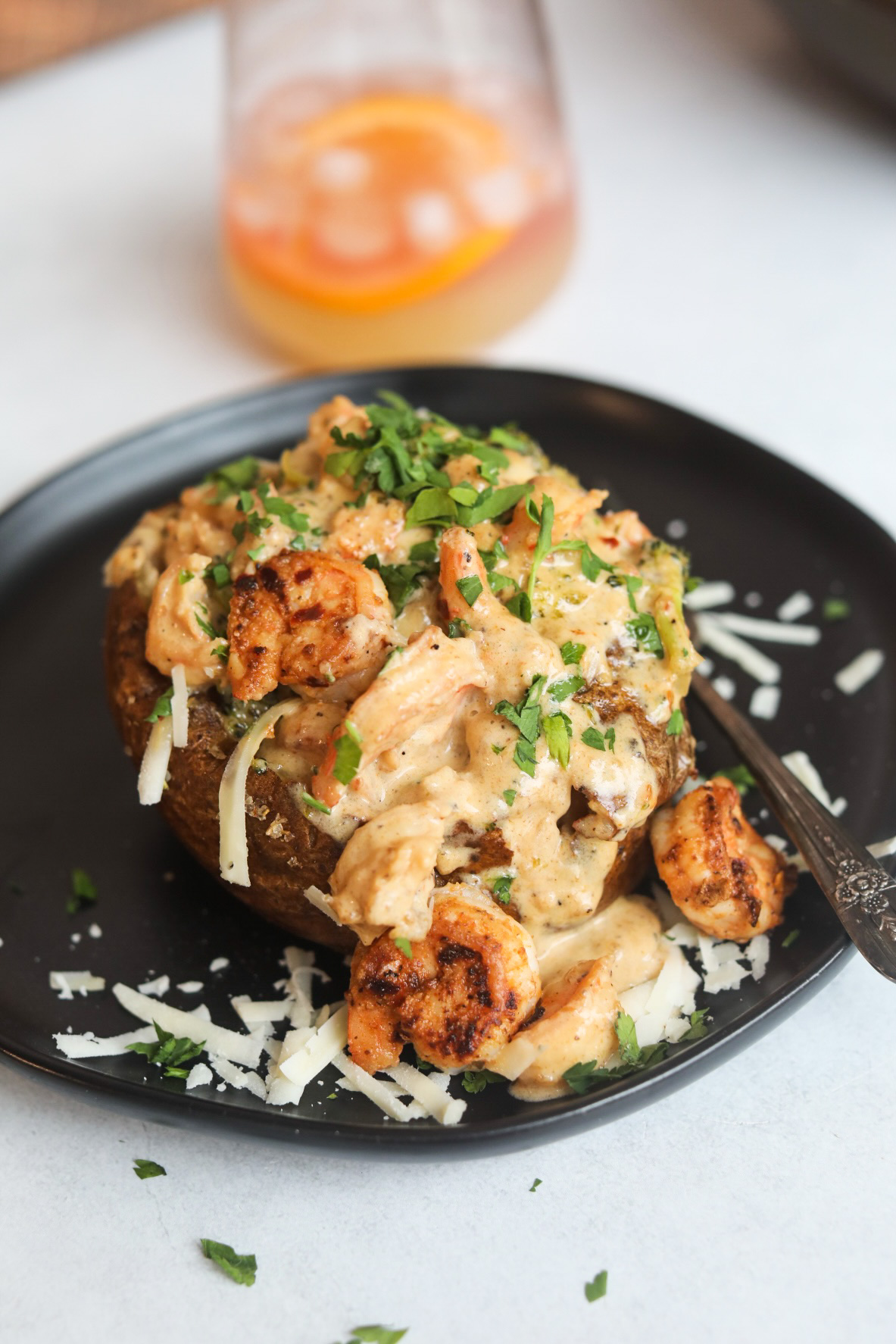 Loaded Shrimp Baked Potato on a black dining plate with antique fork added and an orange cocktail in a stemless wine glass added for styling purposes.