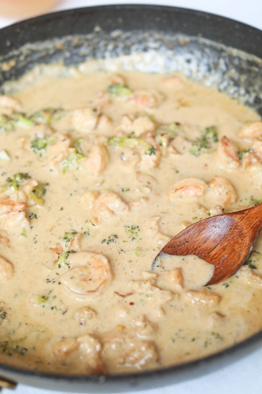 Cajun Shrimp Cream Sauce in a large saute pan with a brown wooden spoon scooping the sauce.