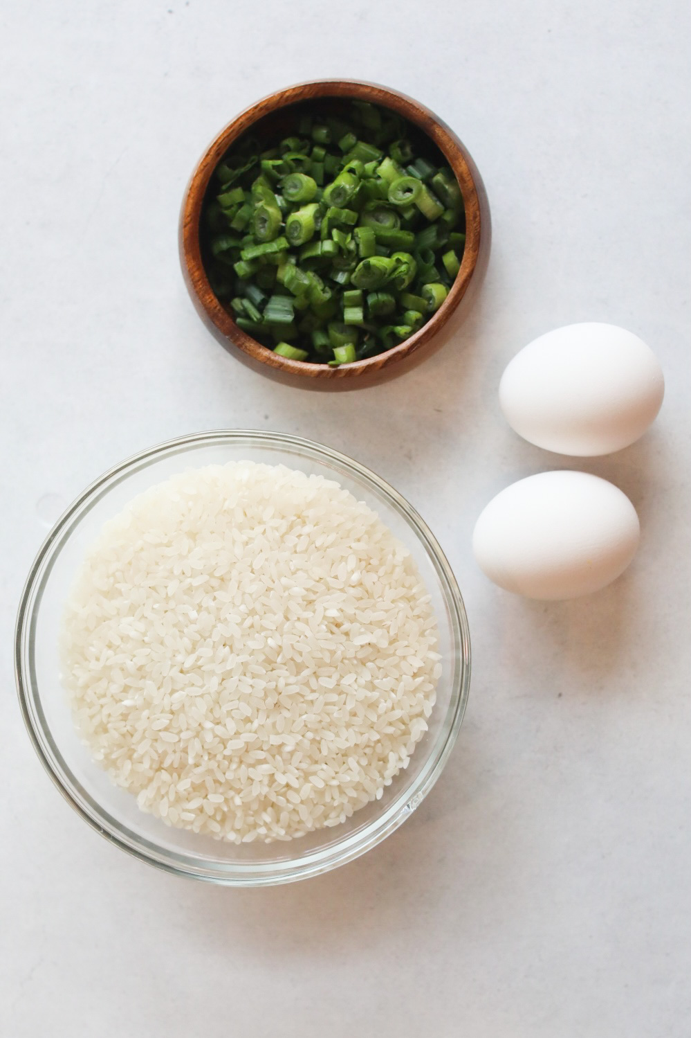 Loco Moco additional ingredients image. Clear bowl of short grain white rice, wooden bowl with chopped green onion and two eggs.