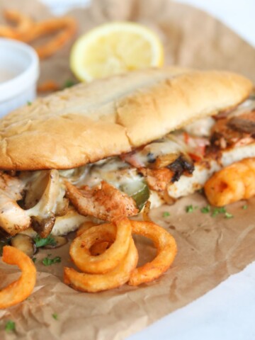 Salmon Cheesesteak with remoulade sauce in a white ramekin. Curly fries and a half of a used lemon is added for styling purposes.