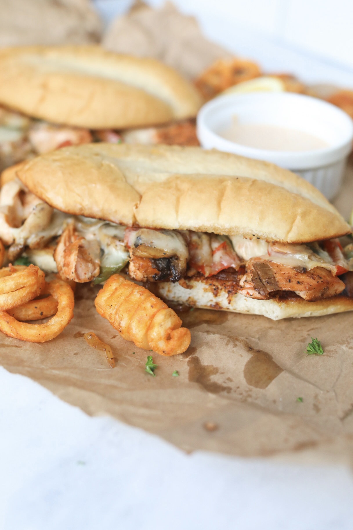 Salmon Cheesesteak with Remoulade Sauce in a white ramekin and curly fries for styling purpsoes.