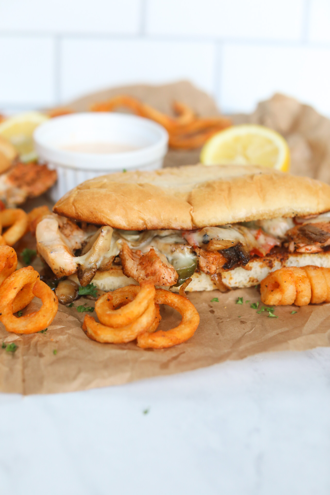 Salmon Cheesesteak with Remoulade Sauce in a white sauce cup with a half squeezed lemon and curly fries for styling purposes.