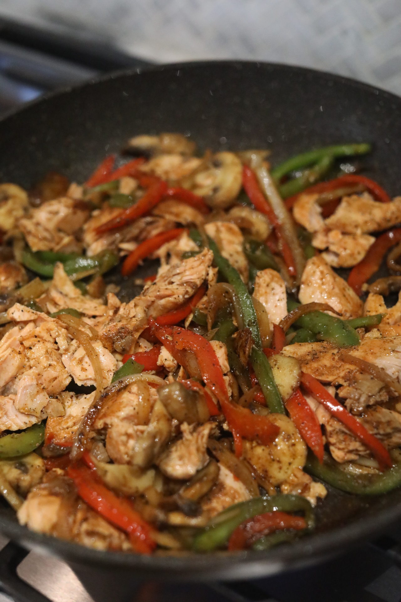 Salmon Cheesesteak ingredients with cooked filling in a black griddle.