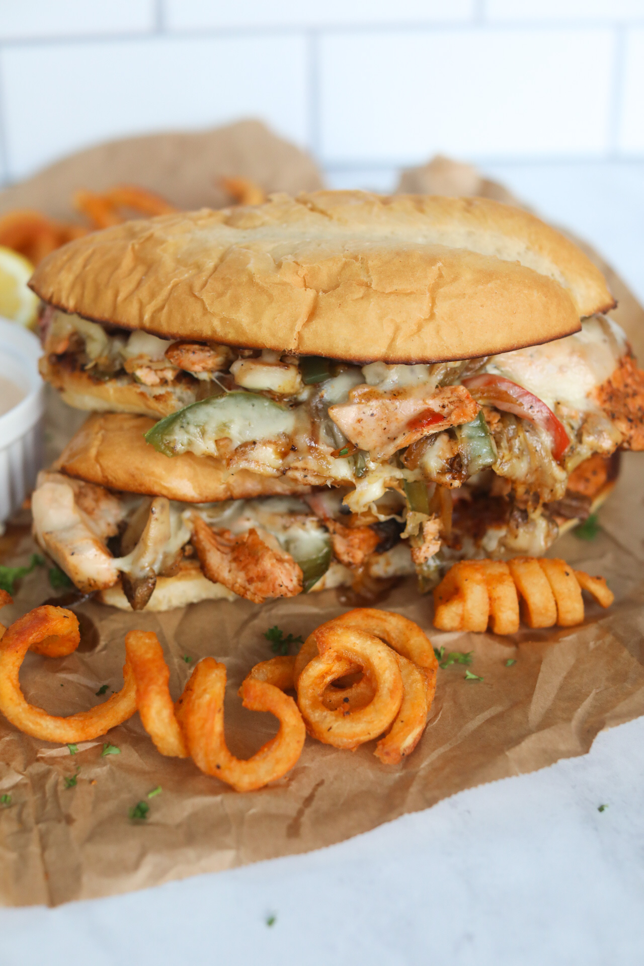 Salmon Cheesesteak with remoulade sauce in white sauce cup and curly fries for styling purposes.